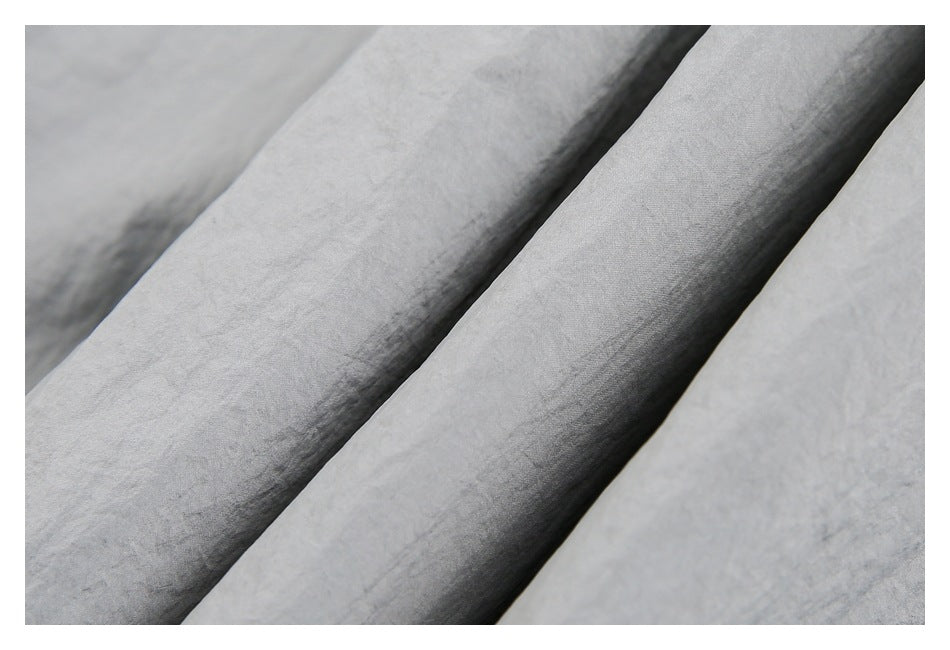 Close-up of light gray garment fabric folded into soft ridges, showing its surface texture.