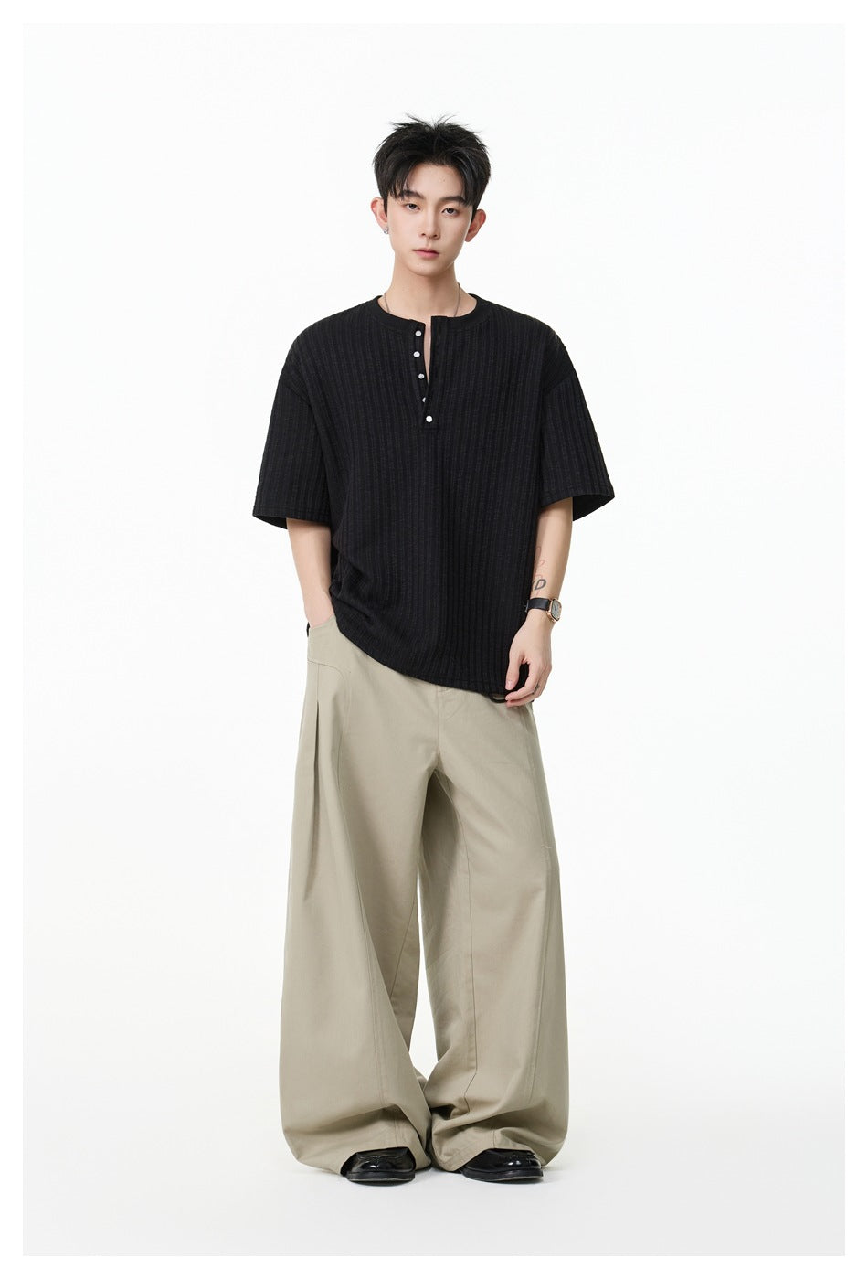 Model wearing a black ribbed short-sleeve henley with beige wide-leg trousers.