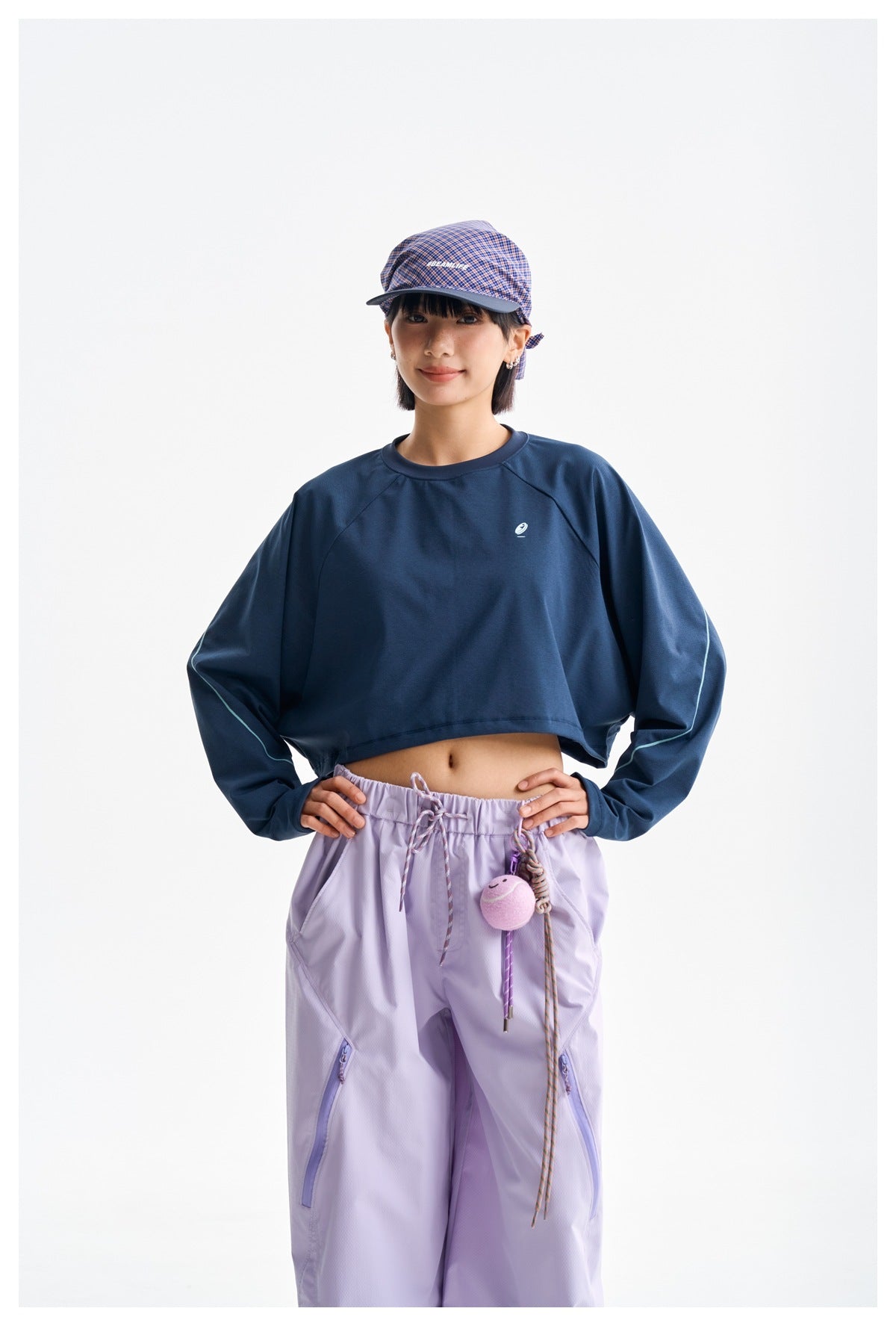 Model wearing a navy cropped long-sleeve top with pale sleeve piping and lilac pants.