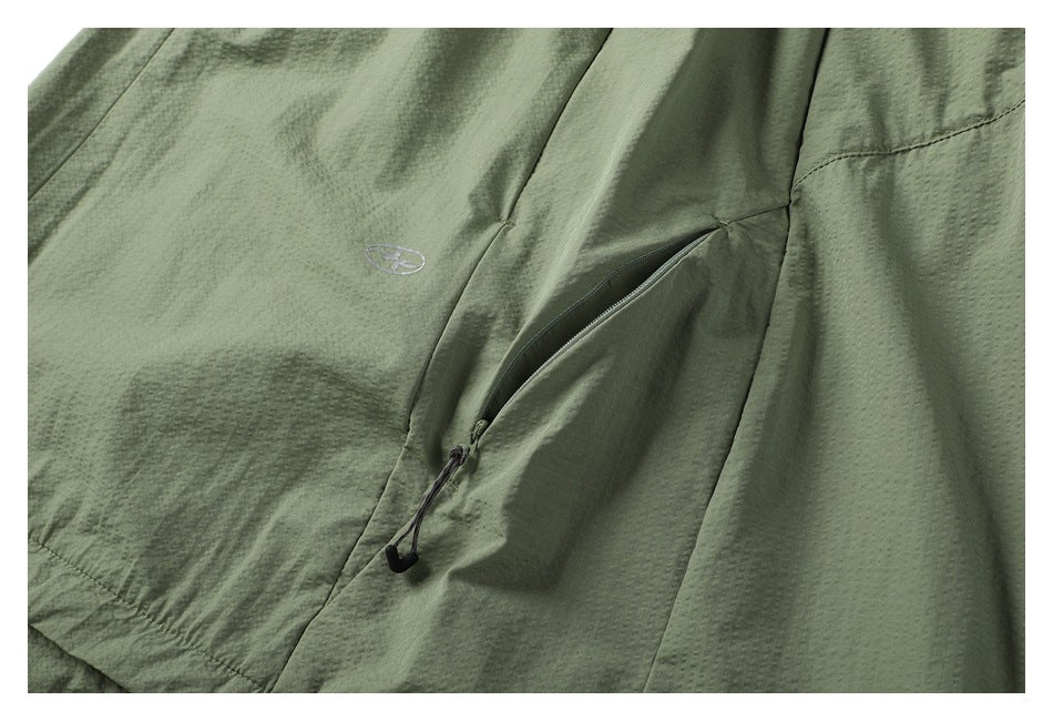 Close-up of a zippered pocket and small embroidered emblem on gray-green fabric.