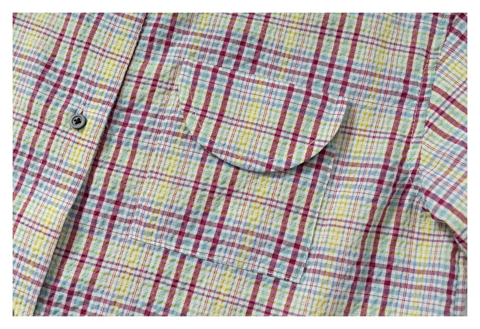 Close-up of a rounded chest pocket and dark button on a multicolor plaid shirt.