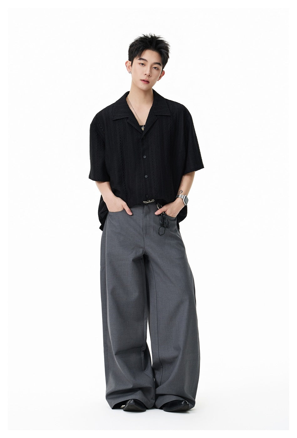 Full-length model wearing a black textured short-sleeve button-up shirt with a notched collar and gray wide-leg trousers.