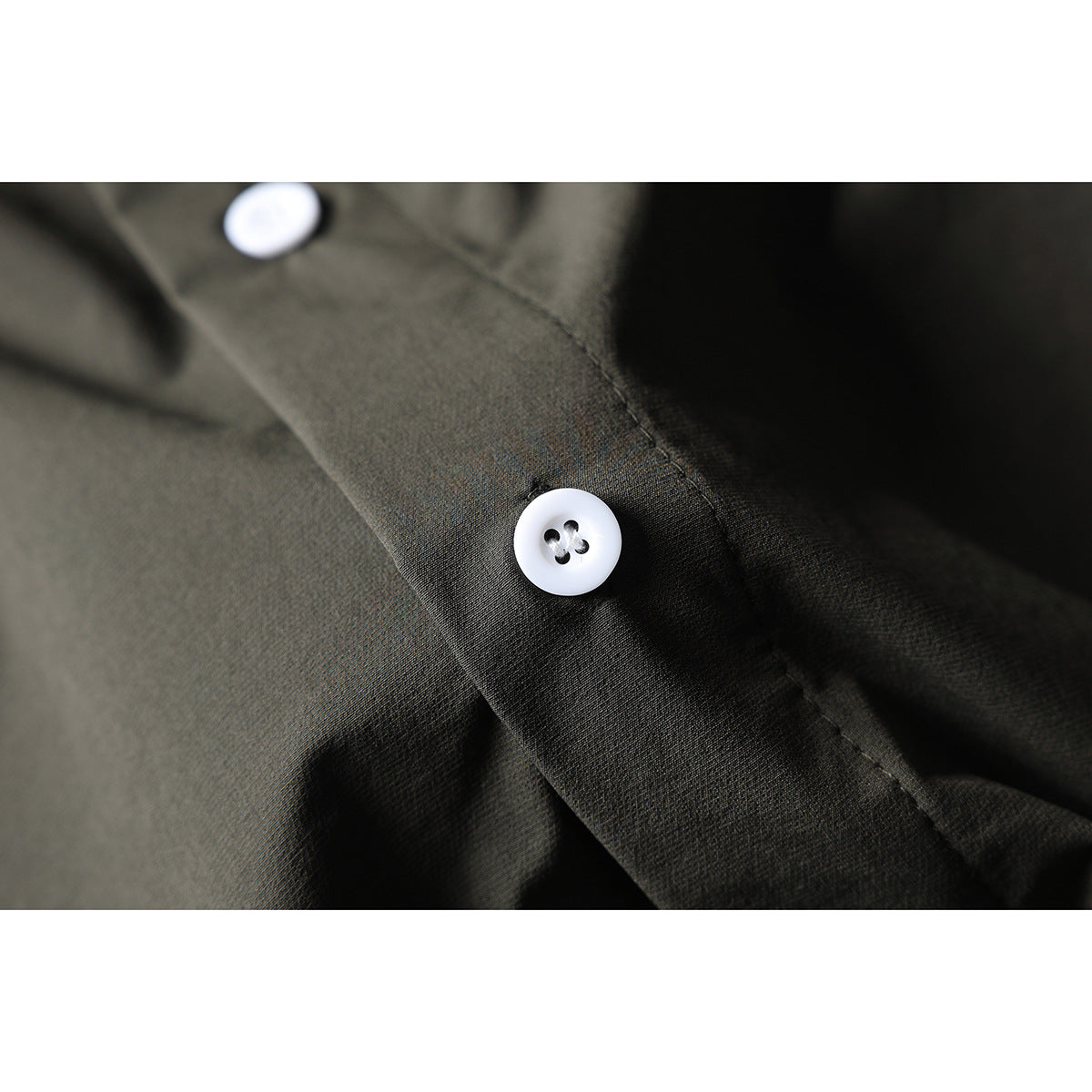Close-up of a white four-hole button on the dark olive-gray shirt fabric.