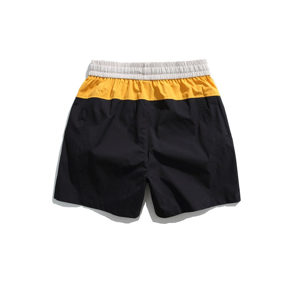 Black shorts back view with orange-yellow yoke panel and light gray elastic waistband, flat lay