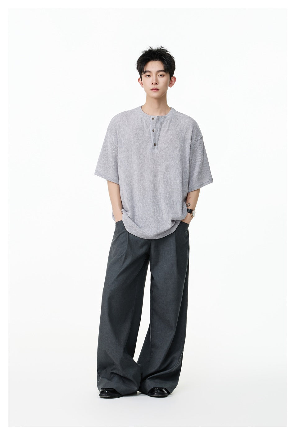 Full-length model wearing a light gray short-sleeve henley shirt, dark wide-leg trousers, and black shoes.