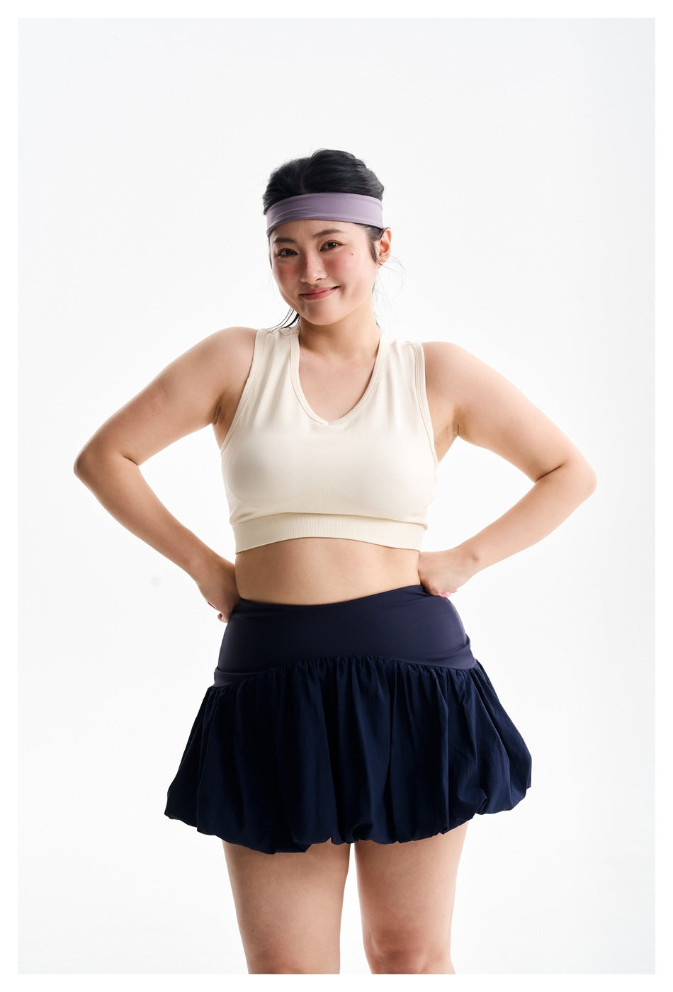Closer front view of a woman wearing an ivory sleeveless crop top and navy bubble-hem athletic skirt.