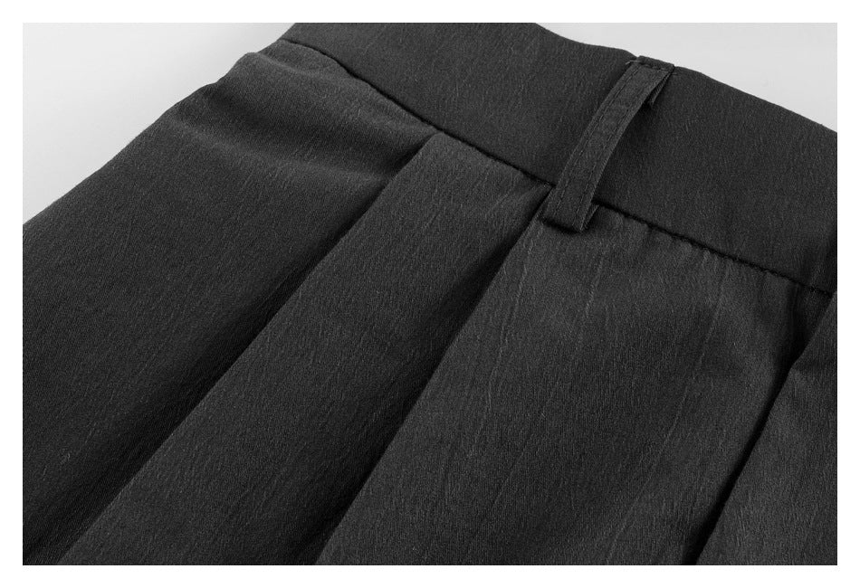 Close-up of black trousers showing a pleat, waistband, and belt loop.