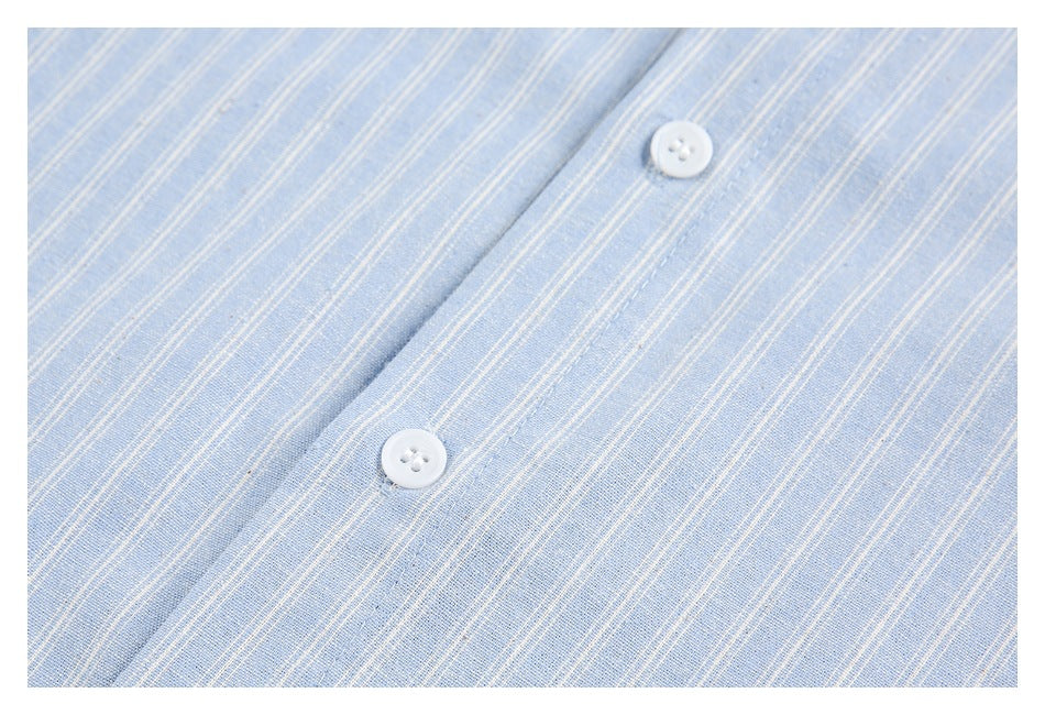 Close-up of a light blue garment with fine white stripes and two white buttons on the placket.