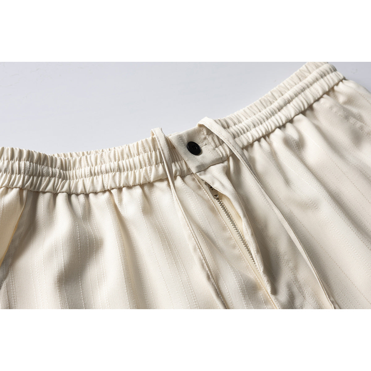Close-up of cream striped shorts showing an elastic waistband, drawstring, black button and zip fly.