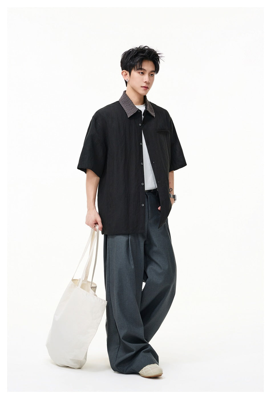Full-length model wearing a black short-sleeve button-up shirt with a textured gray collar and wide charcoal trousers.