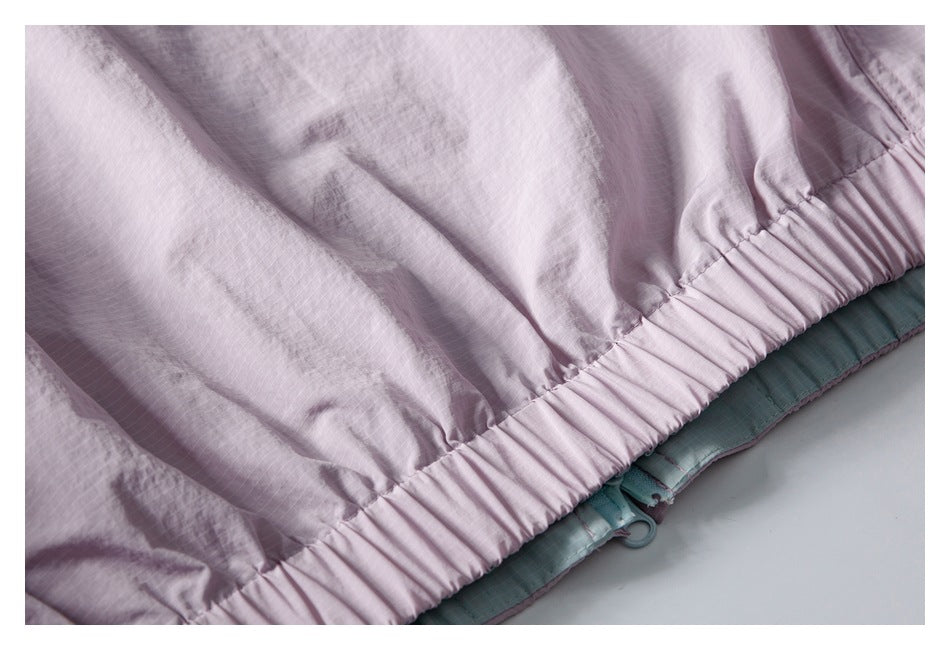 Close-up of a gathered elastic hem on a pale pink garment, with teal fabric visible underneath.