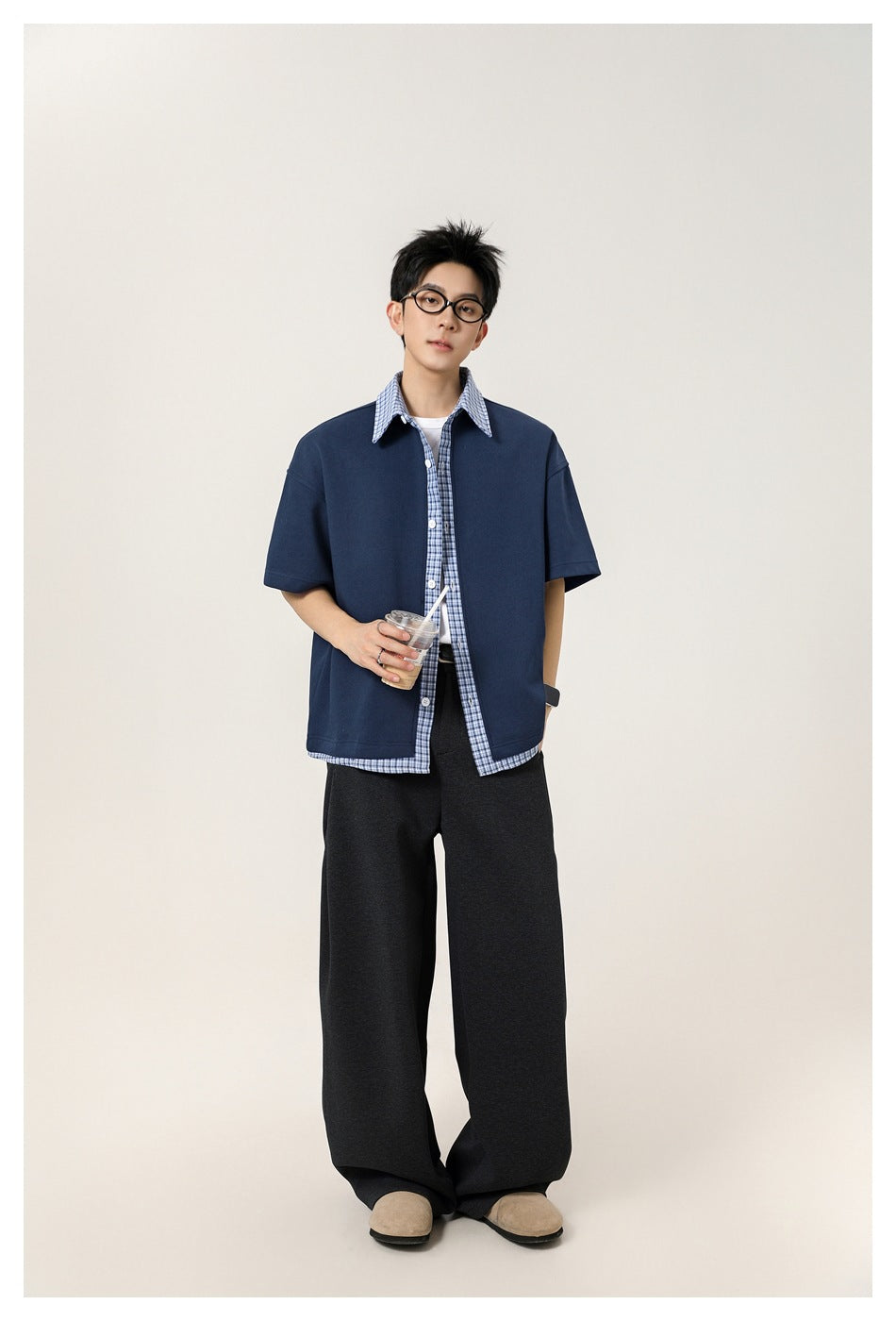 Full-length view of a model wearing a navy short-sleeve shirt with blue plaid trim and wide dark trousers.
