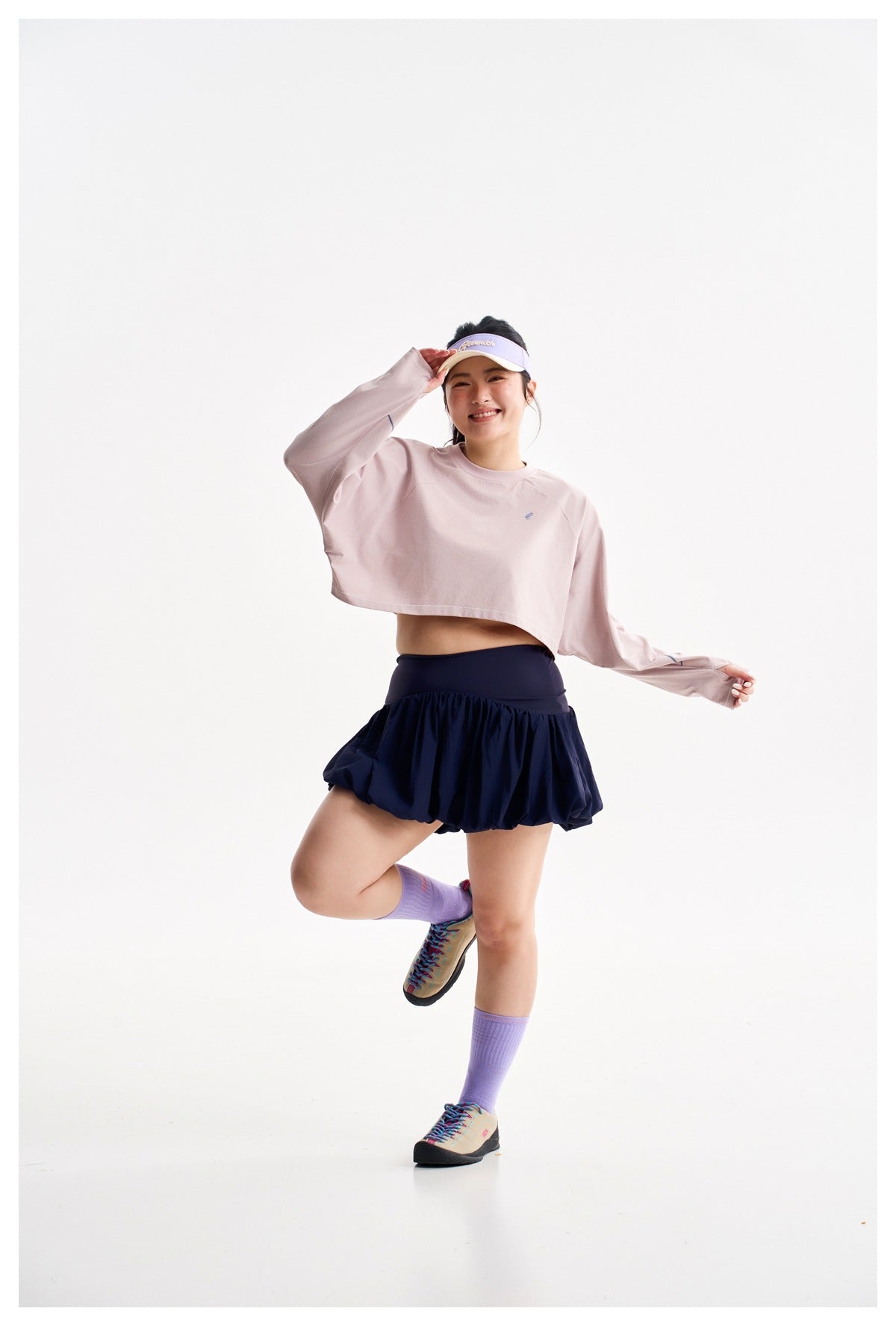 Model wearing a pale pink cropped long-sleeve top and navy bubble-hem skirt, posing with one leg raised.