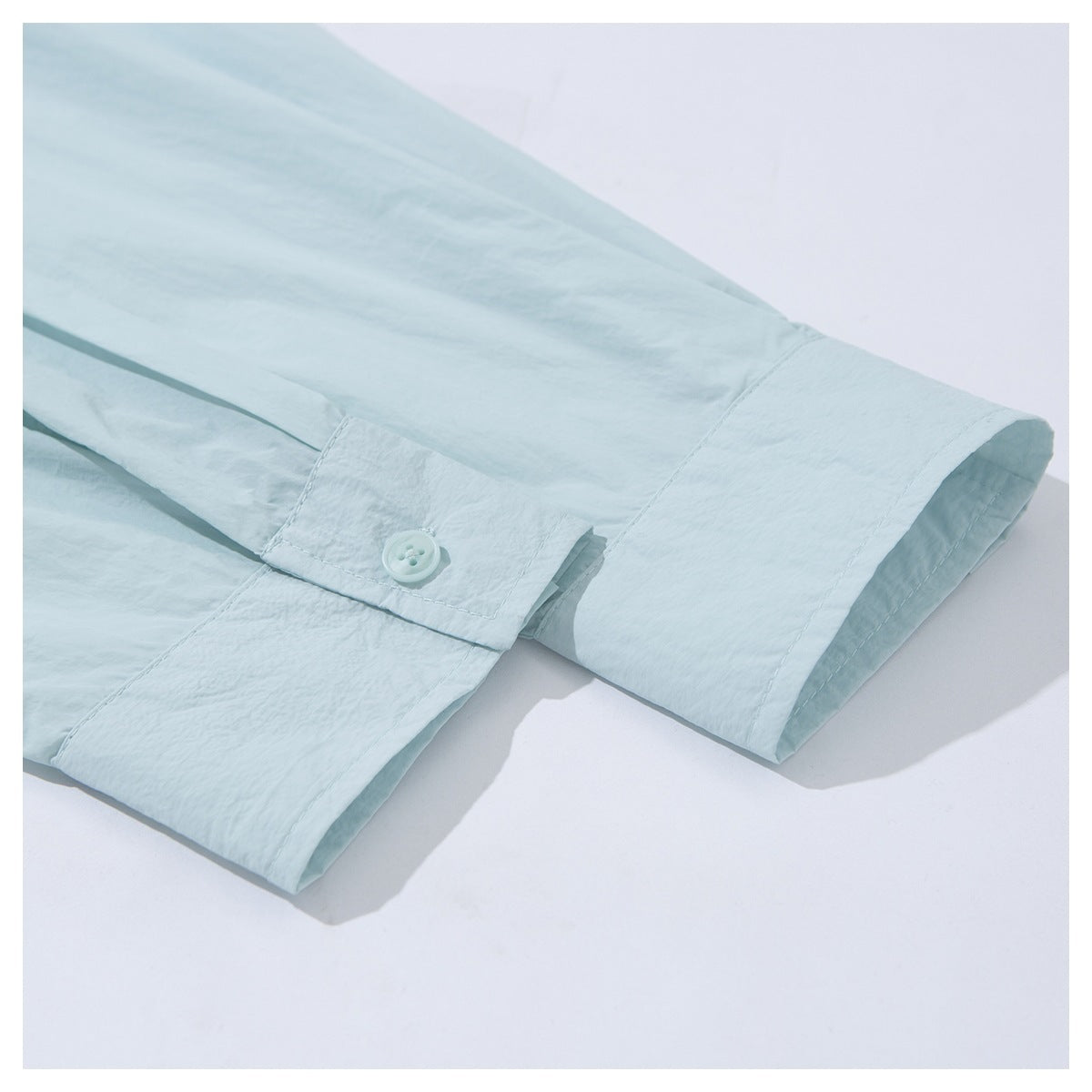 Close-up of a pale mint shirt sleeve and buttoned cuff laid on a white surface.