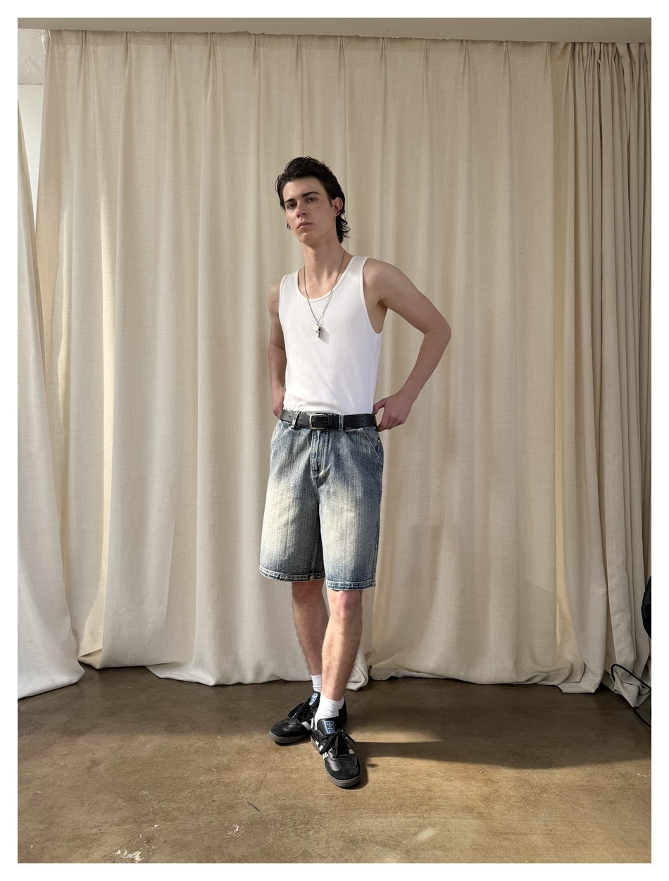 Model wearing faded blue denim shorts with a white tank top and black belt, in a slightly angled front pose.
