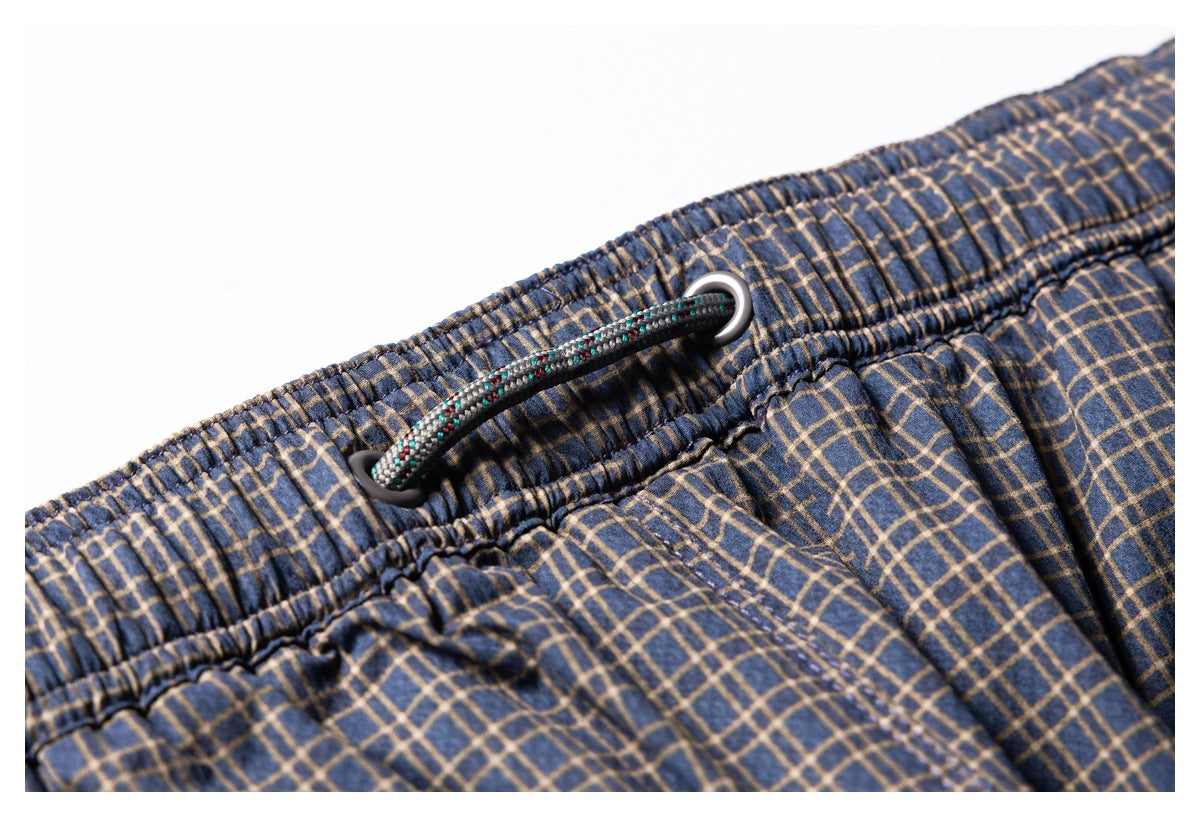 Close-up of the elastic waistband and patterned drawcord on navy plaid shorts.