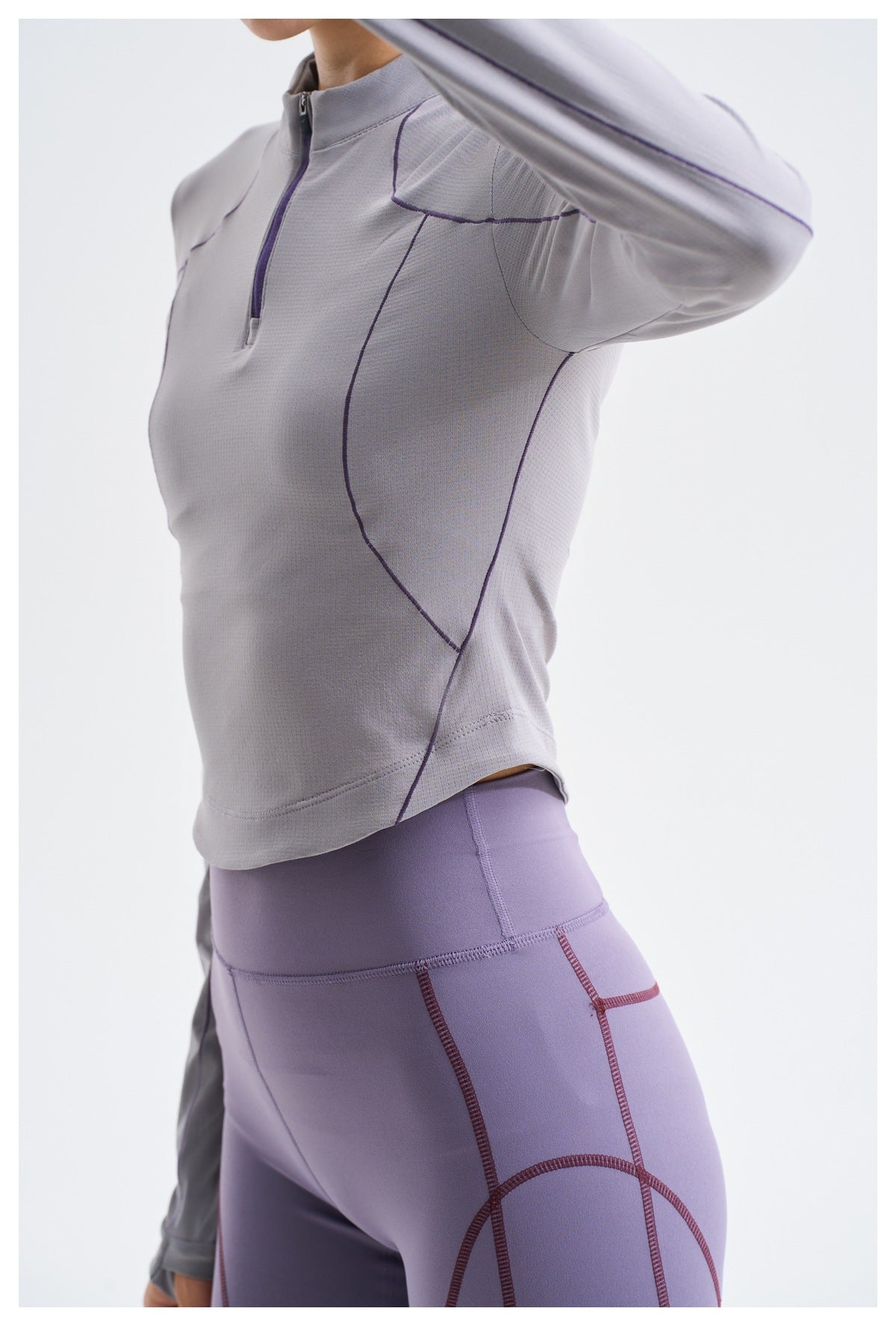 Close side view of a gray-lavender quarter-zip top with purple seam details and purple fitted shorts.