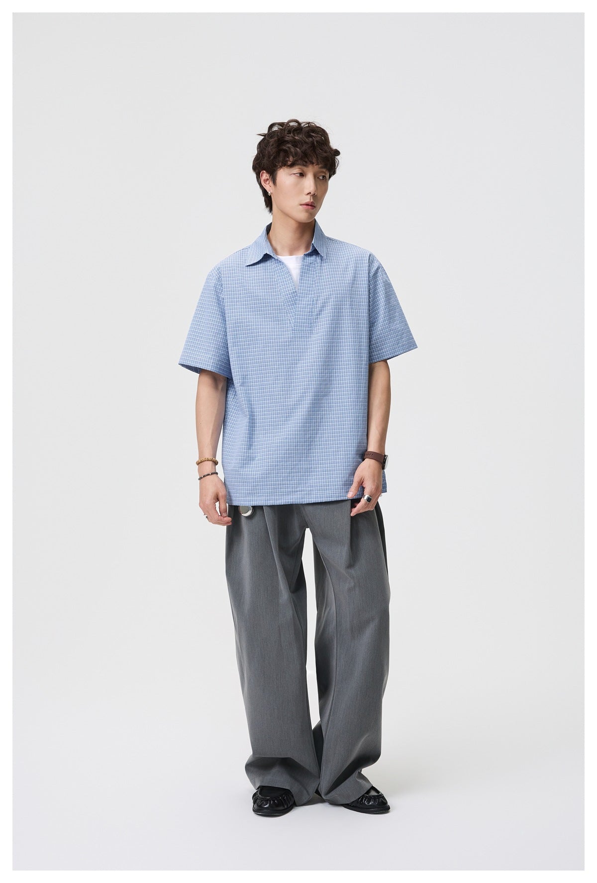 Full-length view of a man modeling a blue-and-white micro-check short-sleeve collared shirt with gray trousers.
