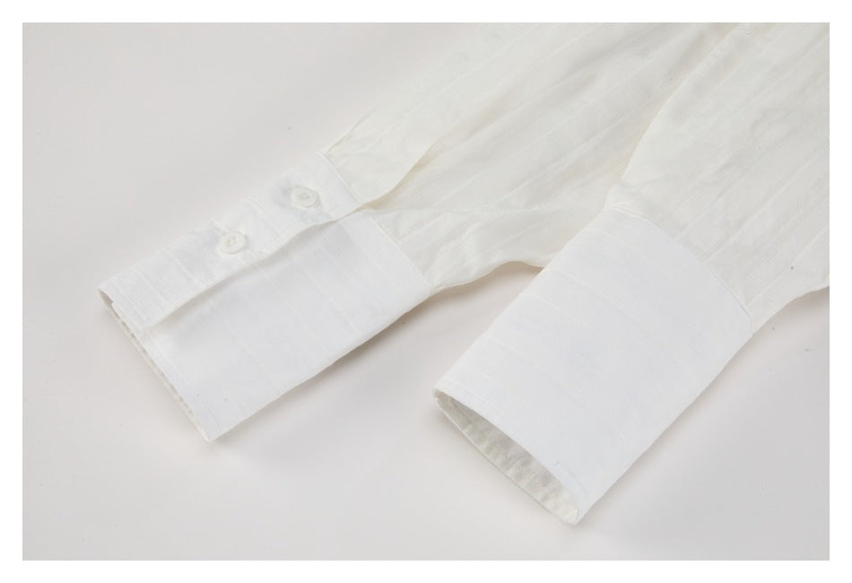 Close-up of the white shirt’s long sleeves and wide buttoned cuffs against a light background.
