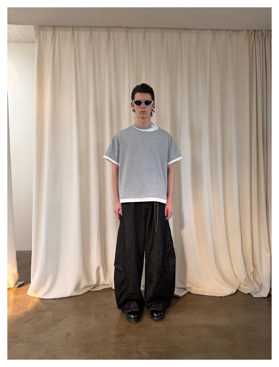 Model wearing a gray layered-look T-shirt with white trim and black wide-leg cargo jeans, front view in front of a curtain