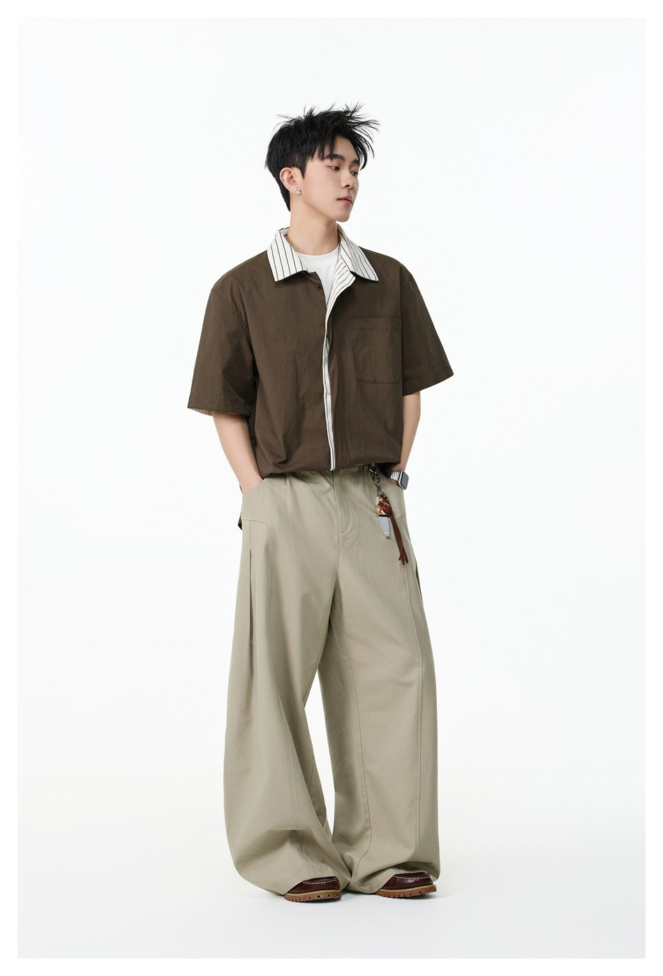 Model wearing a dark brown short-sleeve shirt with a striped collar and placket, paired with wide beige trousers.
