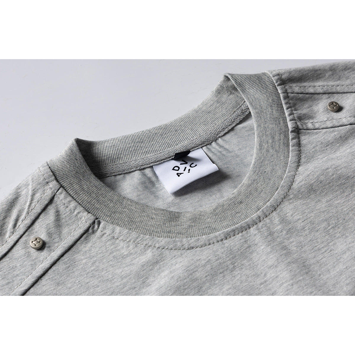 Close-up of a gray crew-neck T-shirt collar, shoulder button tabs and inner label.