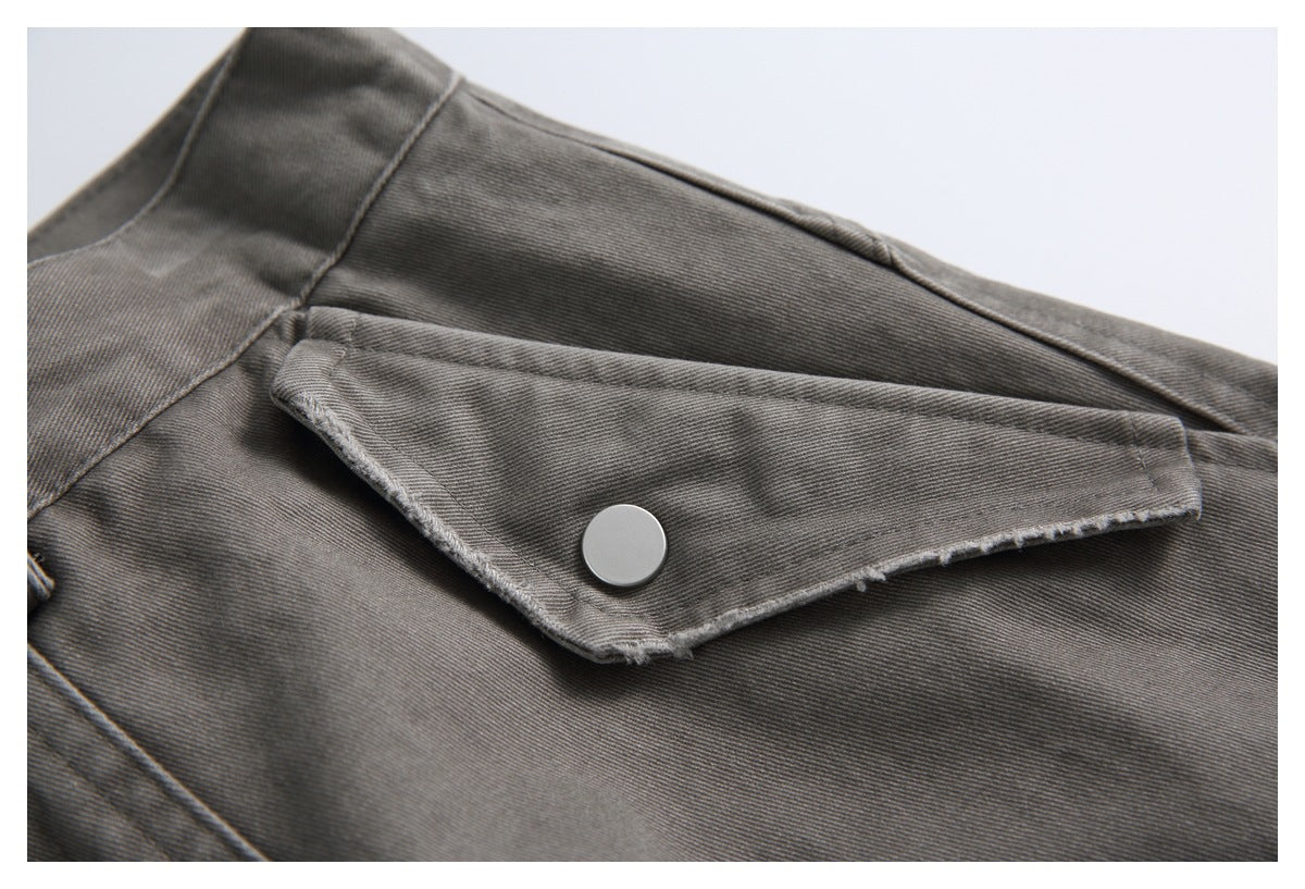 Close-up of charcoal-gray trousers showing a buttoned flap pocket and stitched seams.
