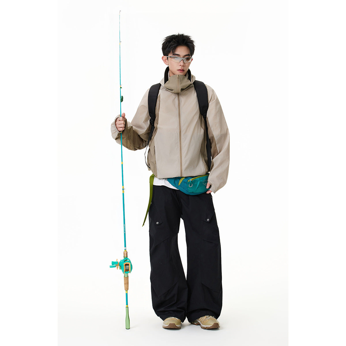 Model wearing a light beige high-collar zip jacket with black trousers and a teal waist bag.