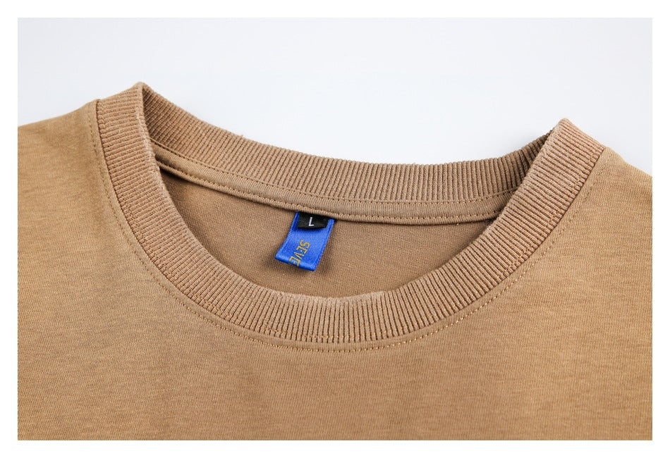 Close-up of the camel-brown T-shirt's ribbed crew neckline, stitching, and blue neck label.
