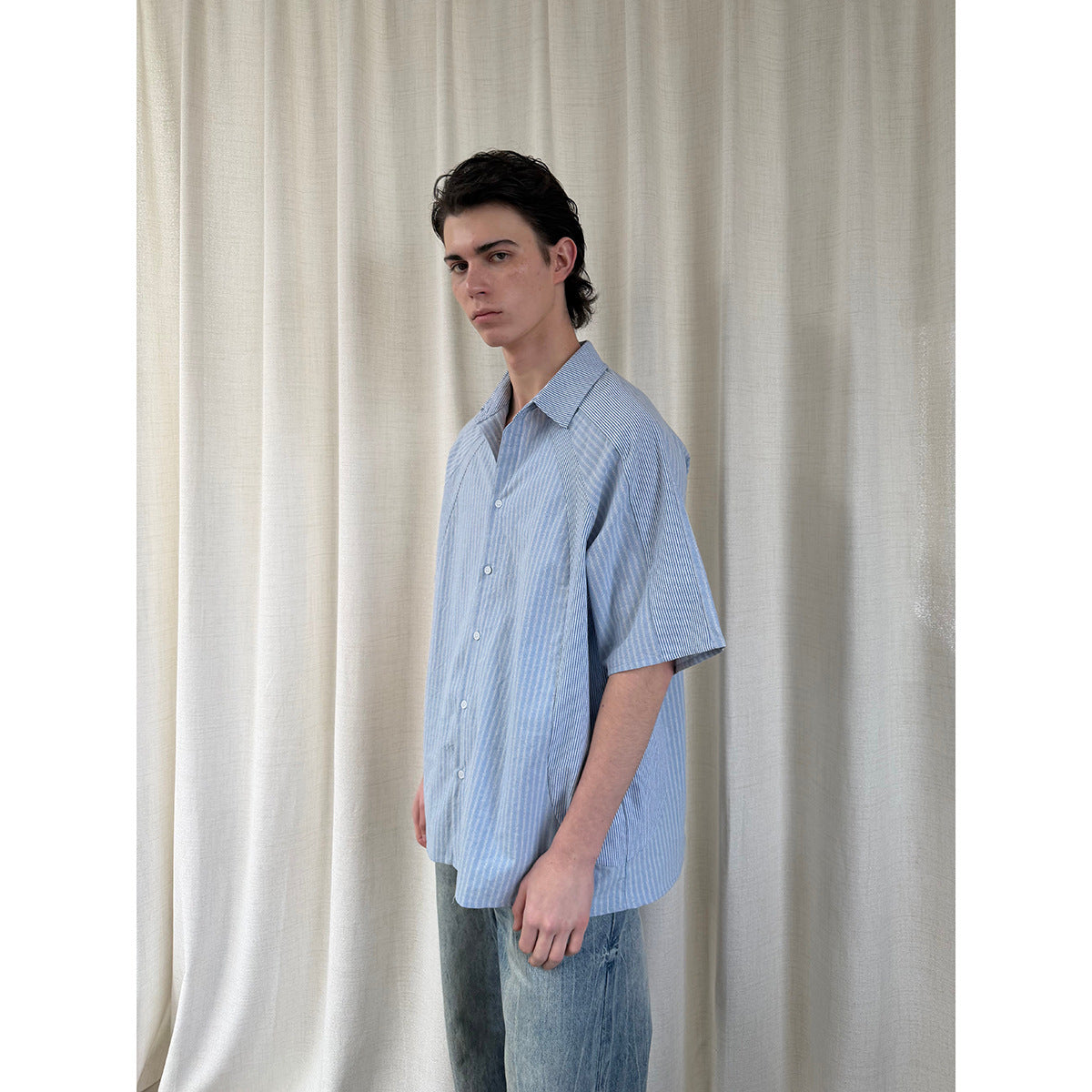 Side view of a model wearing an oversized light blue striped short-sleeve button-up shirt.
