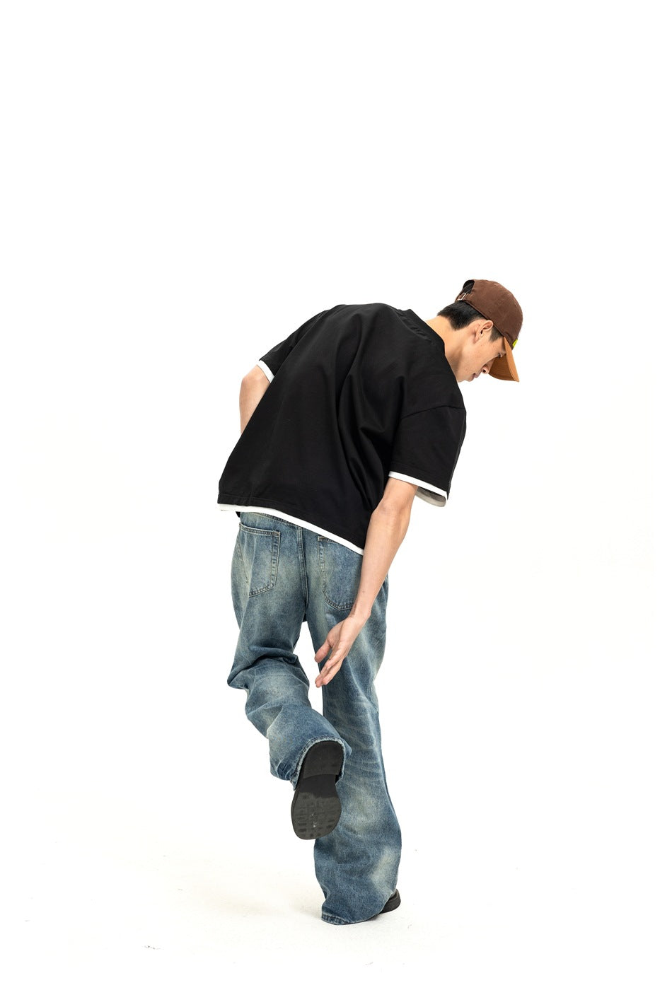Rear view of a model wearing a loose black short-sleeve shirt with white trim and blue jeans.
