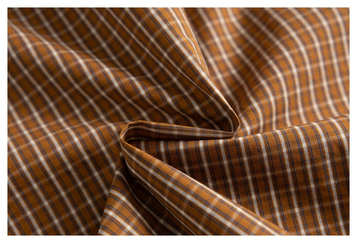 Close-up of draped orange-brown plaid fabric with thin white and dark stripes.