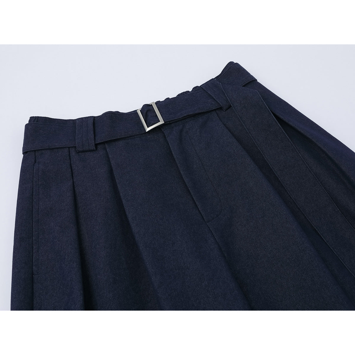 Close-up of dark navy wide-leg trousers showing the pleated waistband, matching belt, and rectangular silver buckle.
