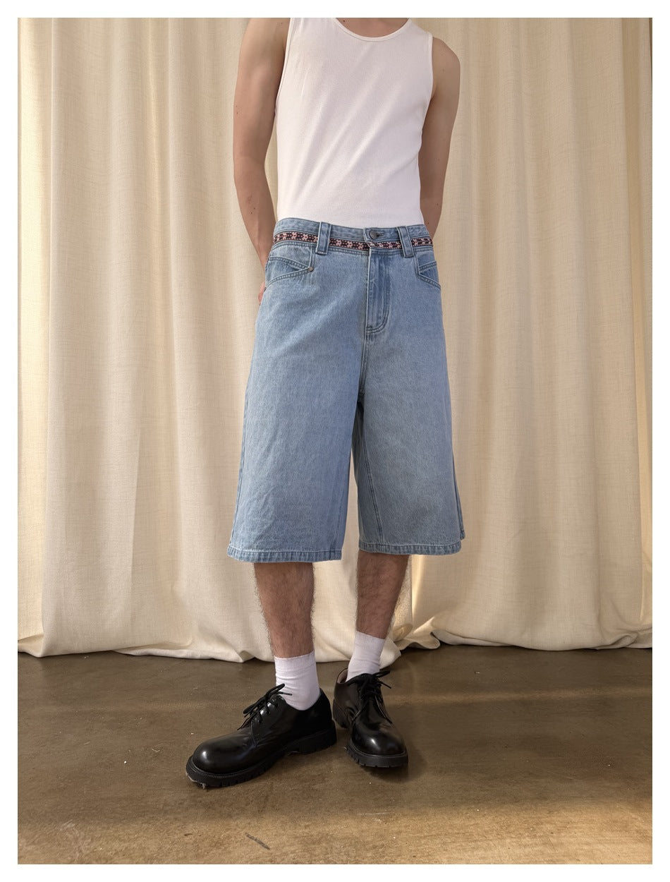 Closer front view of light-wash, wide-leg denim shorts with a red, black and white patterned waistband, worn by a model.