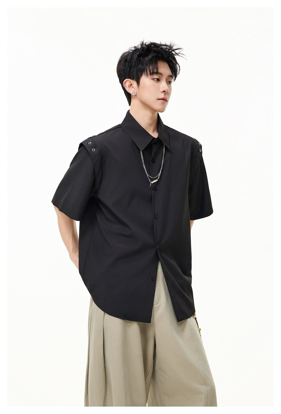 Model wearing a black short-sleeve button-up shirt with metal-eyelet shoulder tabs and beige wide-leg trousers.
