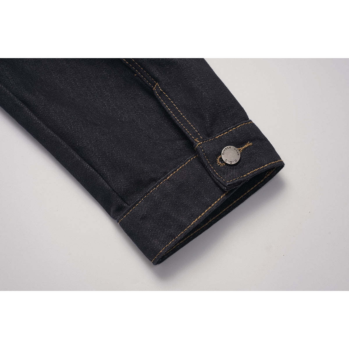Close-up of a dark indigo jacket sleeve cuff with a button closure and contrast stitching.