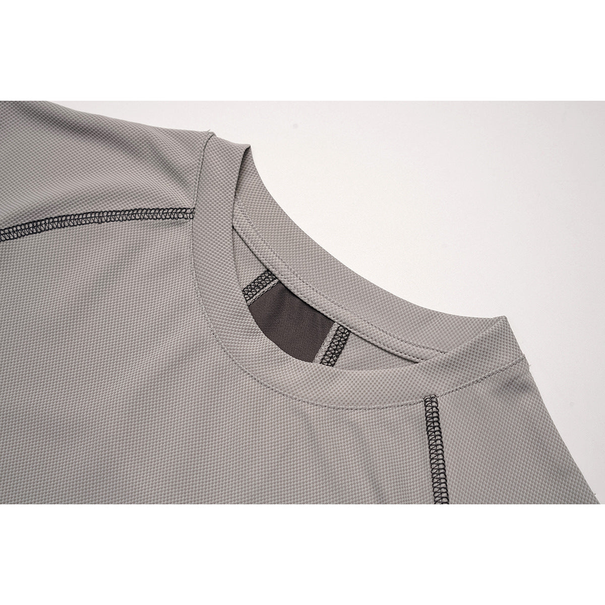 Close-up of the gray top's crew neckline, textured surface and dark overlock stitching.