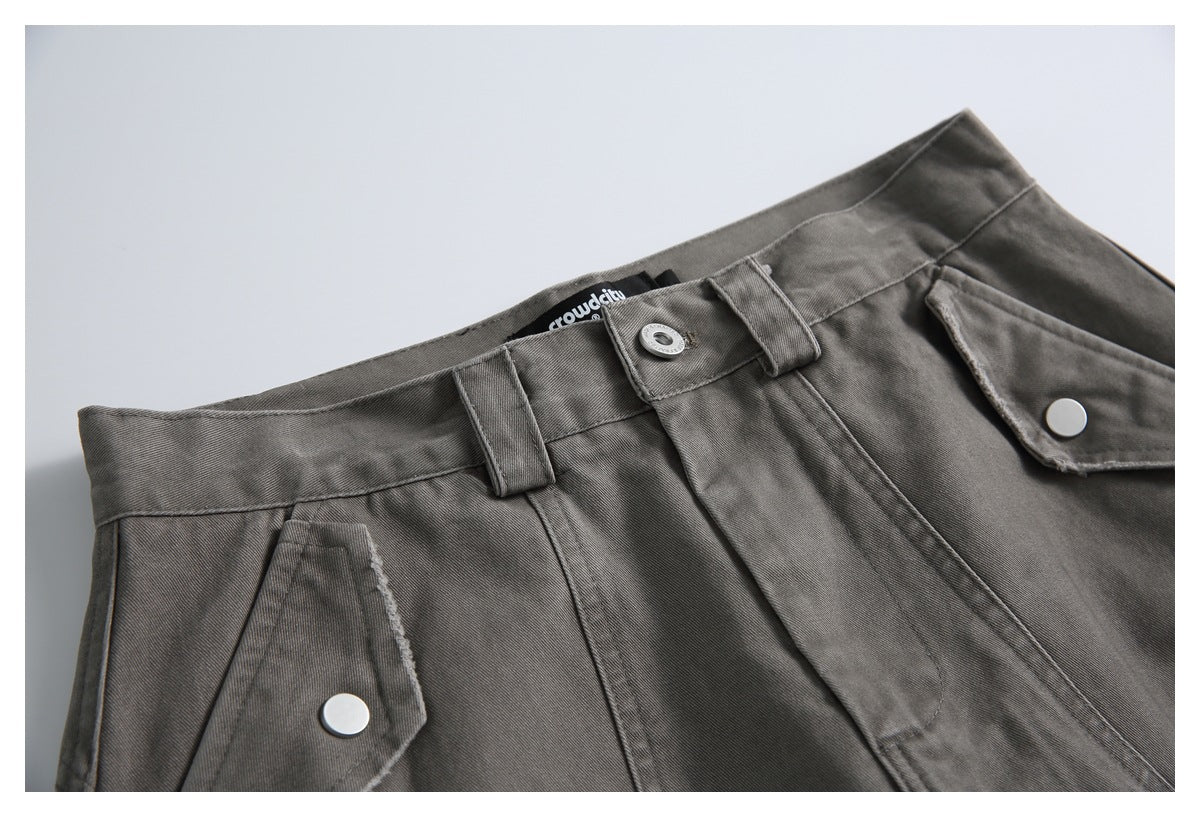 Close-up of gray shorts showing the waistband, belt loops, button, fly, and snap-button pocket flaps.