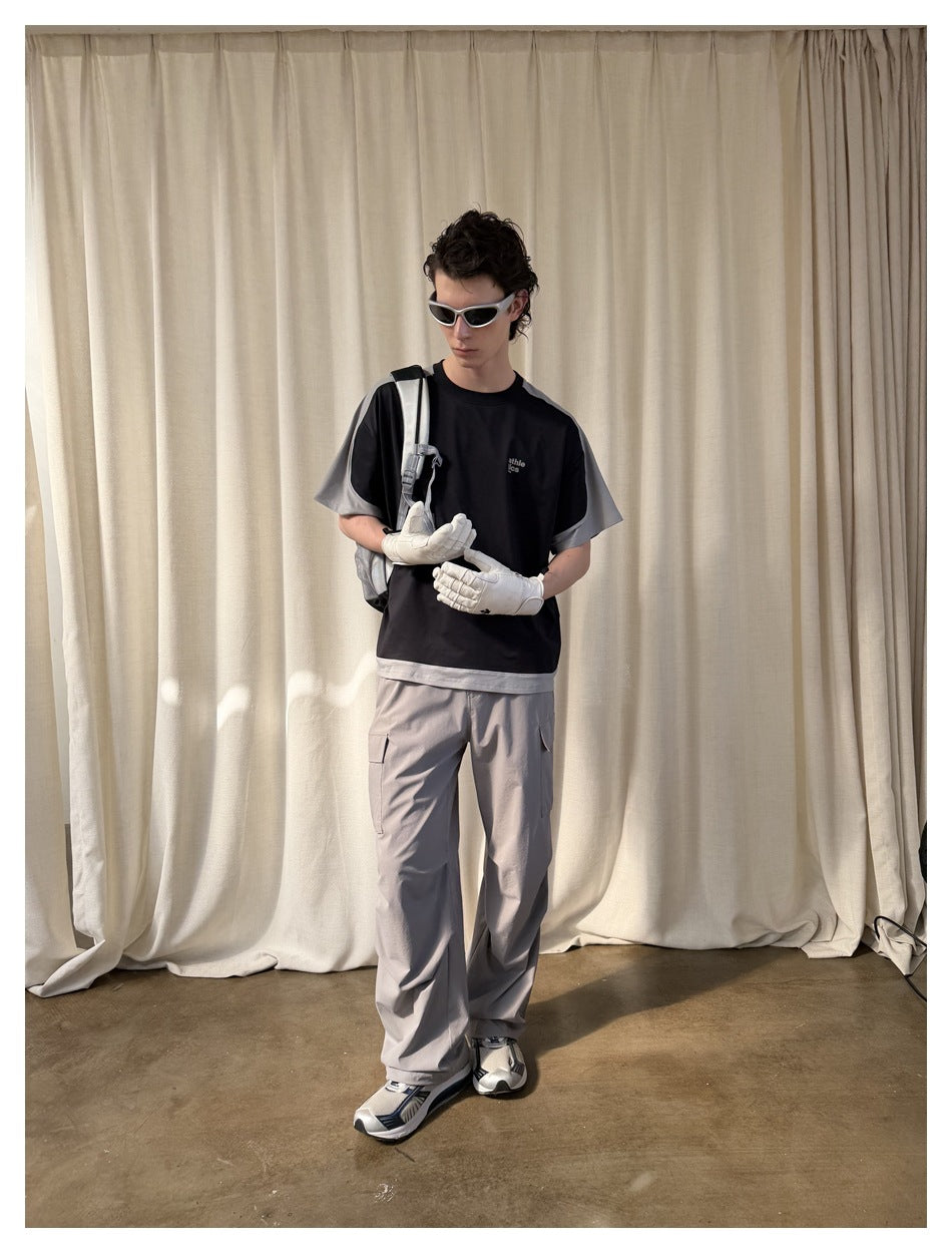 Full-length view of a model wearing a black T-shirt with gray panels and loose gray cargo pants.