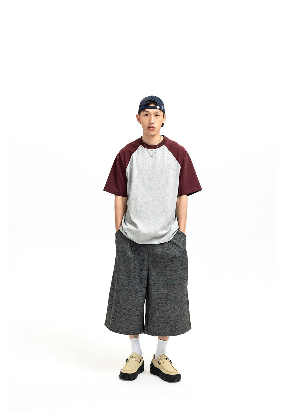 Full-length front view of a model in a light gray T-shirt with burgundy raglan sleeves and plaid shorts.