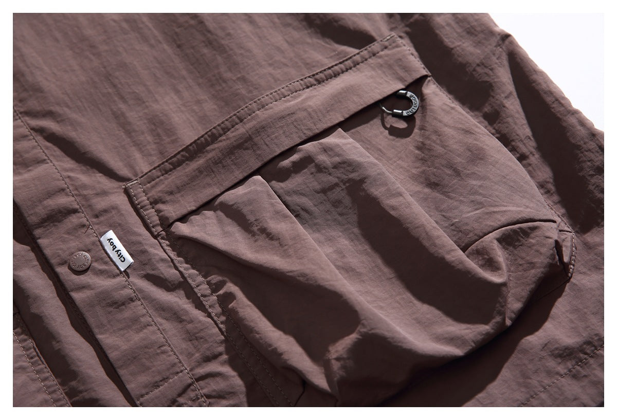 Close-up of a brown jacket's large flap pocket, metal ring detail, snap button, and small sewn label.