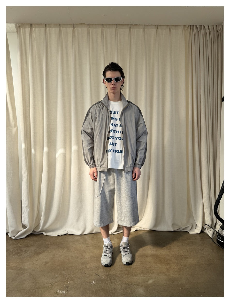 Model wearing the gray two-tone zip jacket open over a white printed T-shirt and gray shorts, full-length view