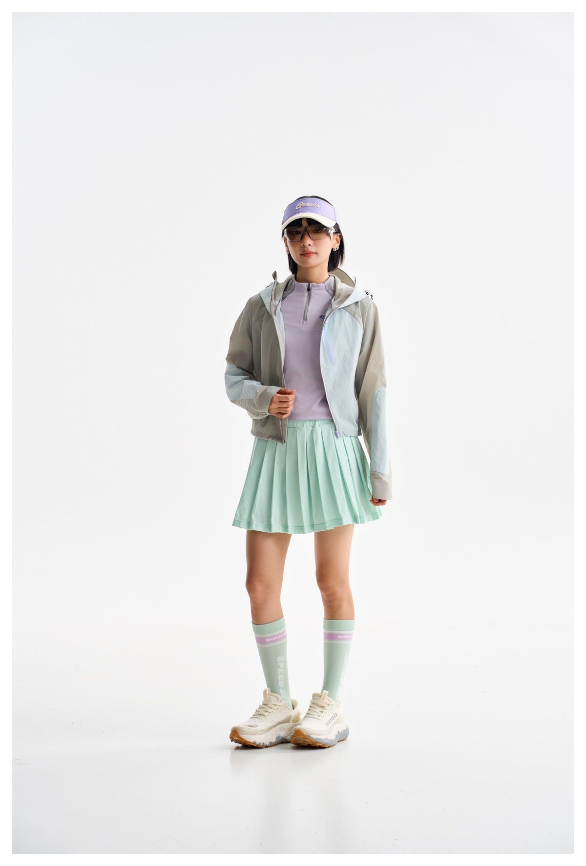 Model wearing a gray color-block hooded jacket, lavender top, and mint pleated skirt.