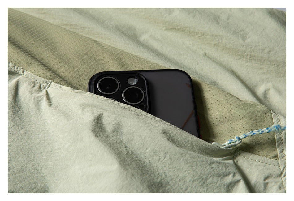 Close-up of a pale sage garment pocket holding a smartphone, showing the textured fabric and blue-and-white cord.