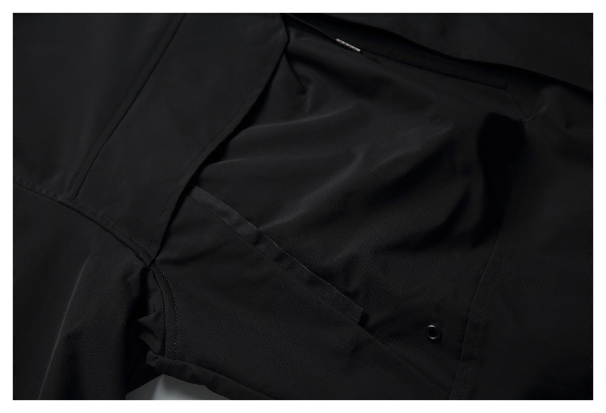 Close-up of a black garment showing stitched panels, a fabric flap, and a small round grommet.