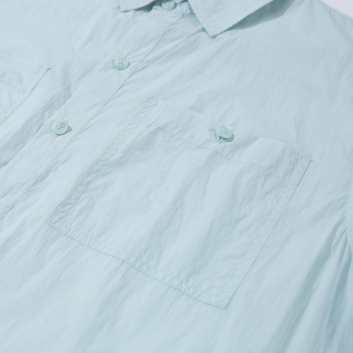 Close-up of a pale aqua shirt’s large square chest pocket and buttoned front placket.