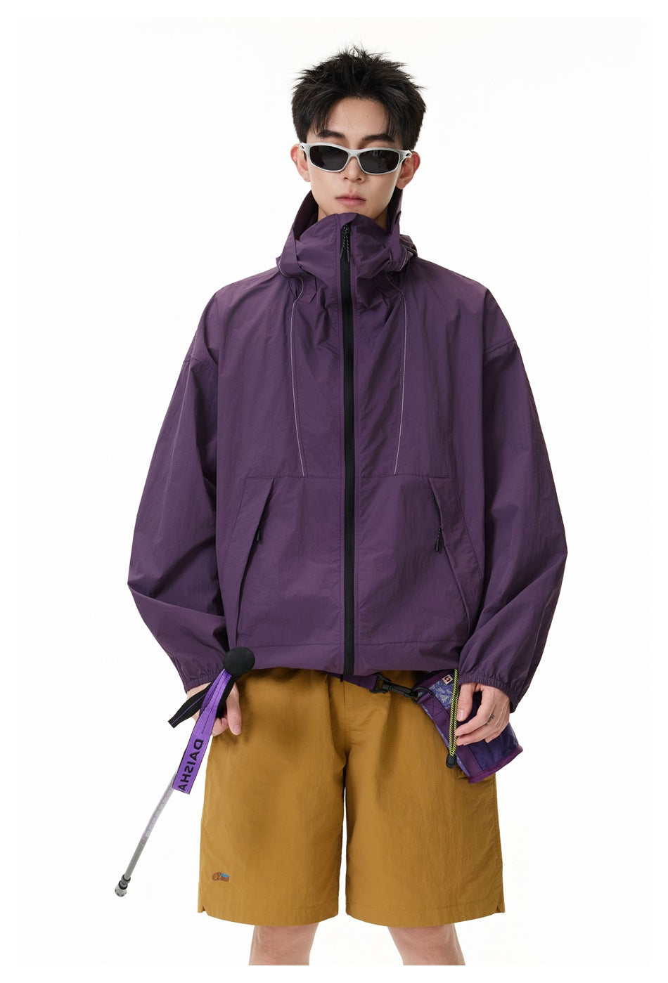 Front view of a model in a plum zip jacket with a high collar and mustard shorts.