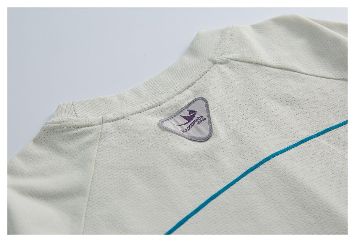 Close-up of an ivory perforated garment with a ribbed neckline, purple logo patch, and teal curved trim.