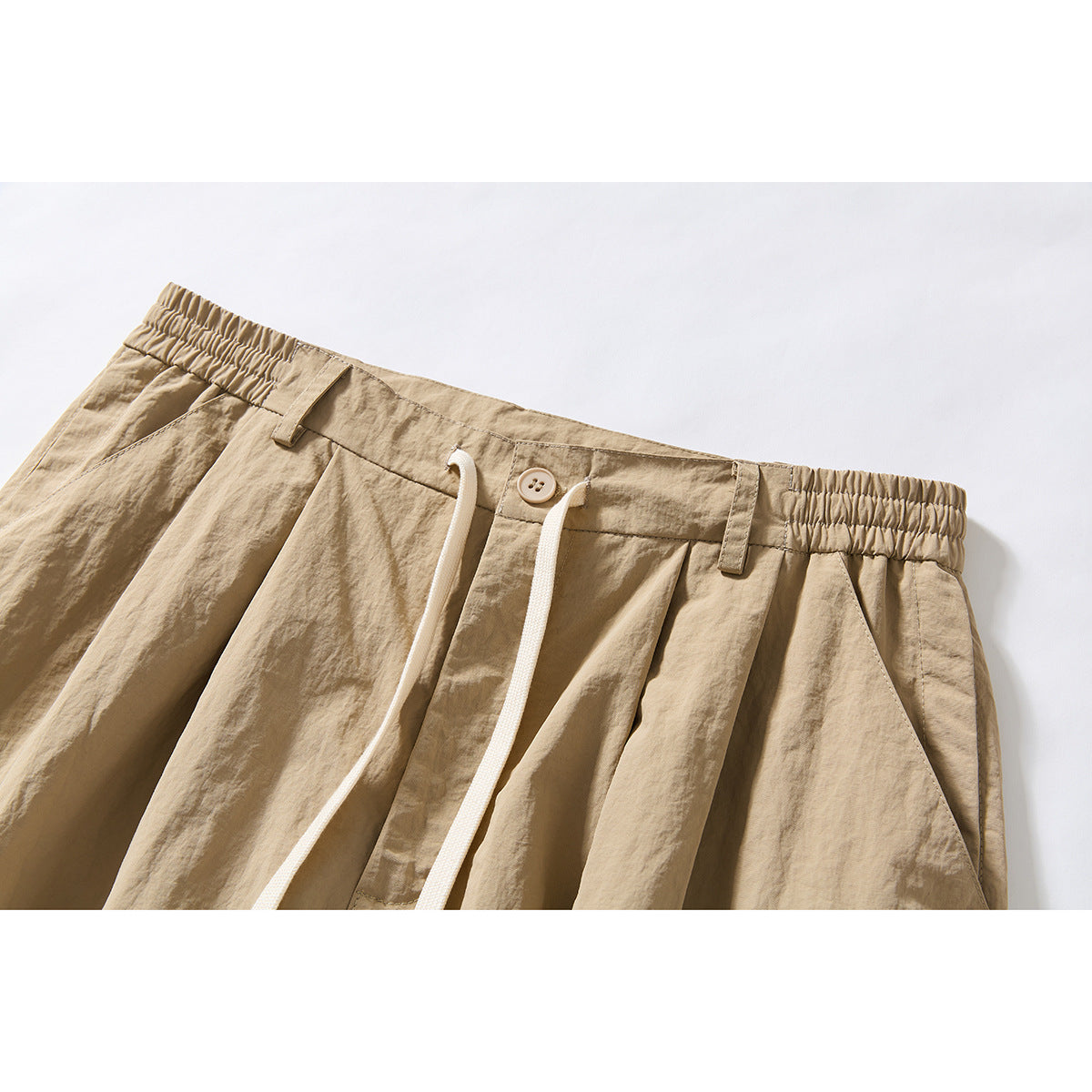 Close-up of beige wide-leg shorts showing the elasticated waistband, button, drawstring, pleats and side pocket.