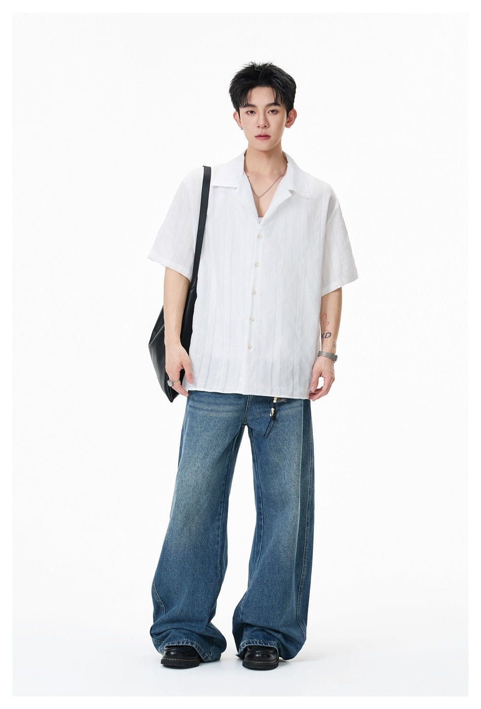 Full-length model wearing a loose white short-sleeve button-up shirt with a wide collar and blue jeans.